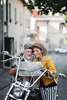 A cheerful senior couple travellers with motorbike in town, using map.