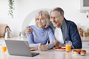 Cheerful senior couple using computer while having breakfast