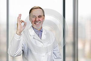 Cheerful senior doctor shows okay gesture sign.