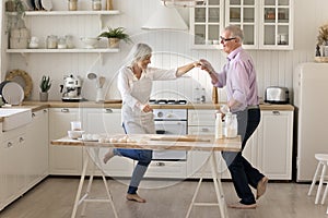 Cheerful senior grey haired couple dancing at kitchen table