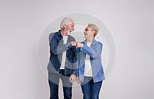 Cheerful senior husband and wife giving fist bumps and looking at each other on white background