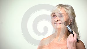 Cheerful senior lady applying powder, positive attitude to age, beauty care