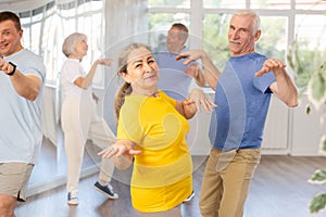 Cheerful senior lady practicing twist with male partner in dance studio