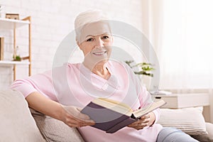 Cheerful senior lady reading book at home