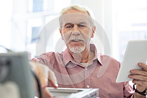Cheerful senior man checking configurations of 3D printer photo