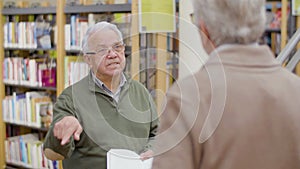 Cheerful senior man discussing book with friend in library