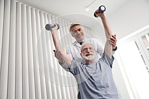 Cheerful senior man doing workout with doctor in clinic