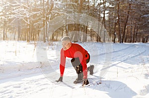 Cheerful senior man ready to run on snowy country road on cold winter day, full length. Active lifestyle concept