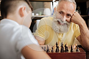 Cheerful senior man smiling at grandson while playing chess