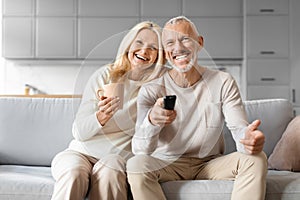 Cheerful senior man and woman watching TV, drinking coffee
