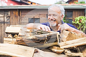 Cheerful senior man work outdoor at home with dry wood ready to fire and warm and heat home in winter season - active retired