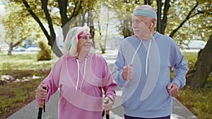 Cheerful senior old couple grandfather, grandmother training Nordic walking, running in summer park