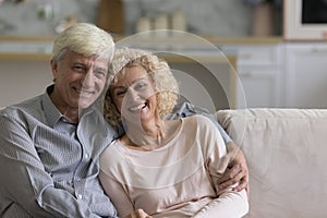 Cheerful senior older couple hugging at home, sitting on sofa