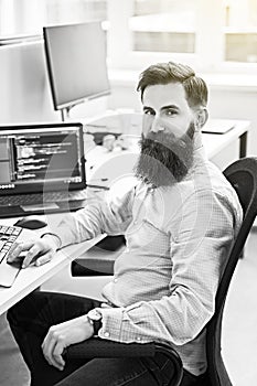 Cheerful senior programmer developer working in IT office, sitting at desk and coding, working on a project in software