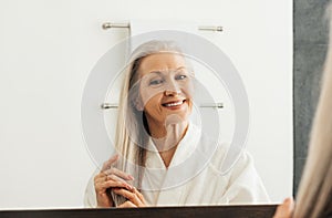 Cheerful senior woman with grey hair looking at a mirror