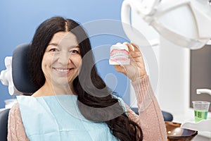 Cheerful senior woman smiling holding teeth mold at the dentist office