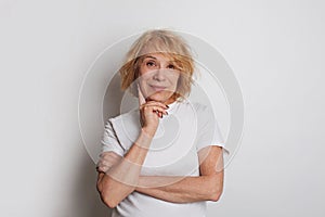 Cheerful senior woman smiling standing against white studio wall background