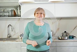 Cheerful senior woman standing in her kitchen smiling