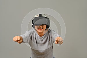 Cheerful senior woman with virtual reality glasses simulating of driving car in VR glasses isolated on white background