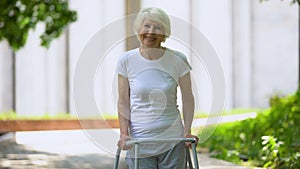 Cheerful senior woman with walking frame looking at camera outdoors, rehab