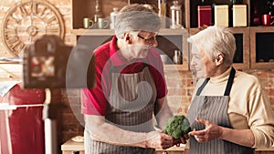 Cheerful seniors recording video at kitchen, panorama