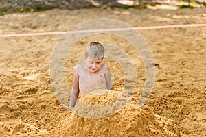 A cheerful seven-year-old boy is buried in the yellow sand on the beach