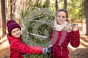 Cheerful siblings hugging a christmas tree, girl showing a chip for the tree, as a provement of legal shopping