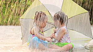 Cheerful siblings little girl having fun in rainy with umbrella at backyard. Children enjoy outdoor activities on hot summer days.