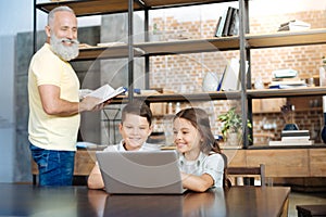 Cheerful siblings watching videos while grandfather reading