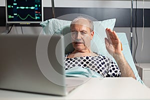 Cheerful sick senior man waving at camera during video conference