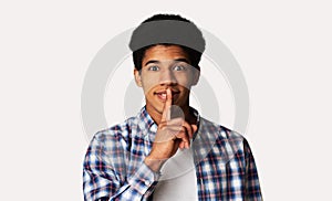 Cheerful silent guy making hush gesture, white background