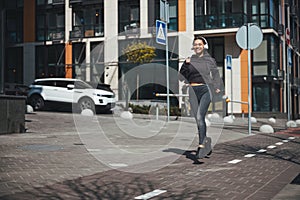 Cheerful slim woman in wireless headphones jogging ahead