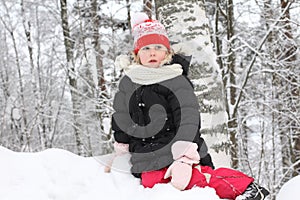 Cheerful small child girl in black winter coat in the snow park