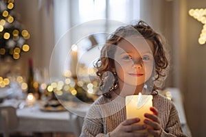 Cheerful small girl standing indoors at Christmas, holding candle.