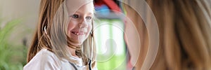 Cheerful small girl using medical stethoscope and looking at doctor with happiness