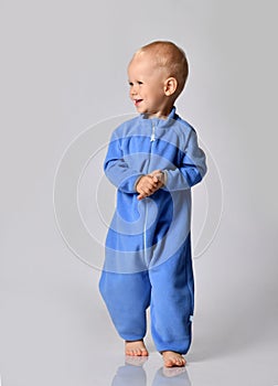 Cheerful smiling baby boy in blue fleece jumpsuit stands looking at free copy space