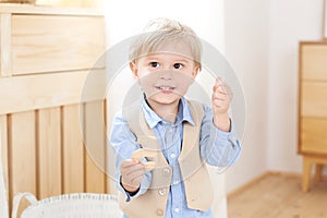 A cheerful and smiling boy holds a figure in his hands. Child in kindergarten. Portrait of fashionable male child. Smiling boy pos