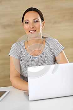 Cheerful smiling business woman working with laptop computer while sitting at the desk in modern office. Middle aged