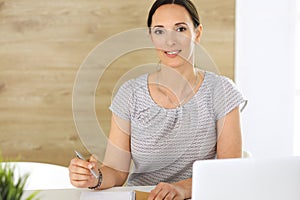 Cheerful smiling business woman working with laptop computer while sitting at the desk in modern office. Middle aged