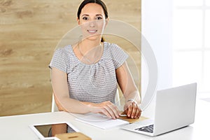 Cheerful smiling business woman working with laptop computer while sitting at the desk in modern office. Middle aged
