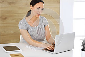 Cheerful smiling business woman working with laptop computer while sitting at the desk in modern office. Middle aged