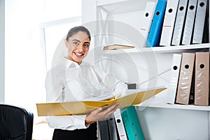 Cheerful smiling businesswoman standing and holding yellow folder