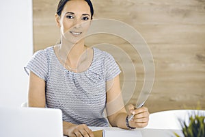 Cheerful smiling businesswoman working with laptop computer while sitting at the desk in modern office. Middle aged