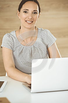 Cheerful smiling businesswoman working with laptop computer while sitting at the desk in modern office. Middle aged