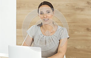 Cheerful smiling businesswoman working with laptop computer while sitting at the desk in modern office. Middle aged