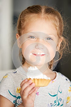 Cheerful smiling child girl eating a delicious cake and showing thumbs up. mouth in cream.