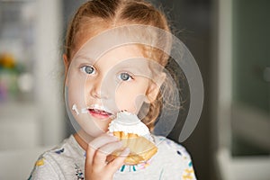 Cheerful smiling child girl eating a delicious cake and showing thumbs up. mouth in cream.