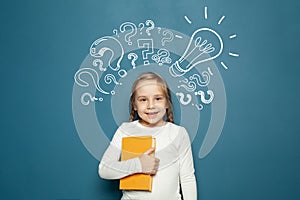 Cheerful smiling child school student with yellow book, lightbulb and chalk question marks. Brainstorm, problem and solution