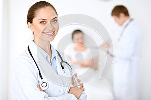 Cheerful smiling female doctor on the background with physician and his patient in the bed