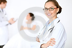 Cheerful smiling female doctor on the background with physician and his patient in the bed